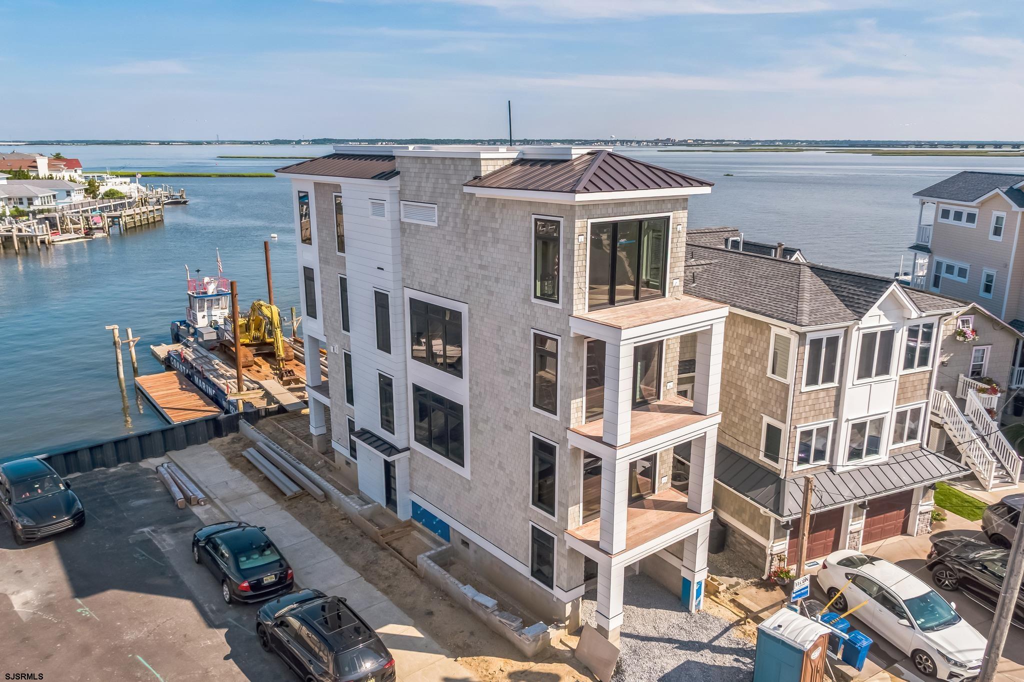 Welcome to 233 W. 17th Street—a striking new construction bayfront residence offering the ultimate in luxury coastal living. Nestled directly on the open bay in Ocean City’s sought-after waterfront neighborhood, this custom-designed 4-bedroom, 4.5-bathroom single-family home is where timeless elegance meets modern comfort. Designed with seamless indoor-outdoor living in mind, this home features an open-concept floor plan with soaring ceilings, walls of glass, and panoramic bay views from every level. The gourmet kitchen is a dream for entertaining—complete with a waterfall-edge quartz island, custom cabinetry, premium appliances, and designer lighting. Step outside to multiple waterfront decks, a beautifully landscaped yard, and your private dock—perfect for boating, fishing, paddleboarding, or simply soaking in the sunsets. The primary suite is a private oasis featuring a spa-inspired bath, oversized walk-in closet, and a private terrace overlooking the water. Additional highlights include: • Private elevator • Rooftop deck with sweeping bay views • Garage parking & ample storage • NuCedar siding, standing seam metal roof, and Marvin Modern windows • Thoughtfully designed indoor/outdoor flow with multiple entertaining spaces Located just minutes from the beach, boardwalk, and downtown Ocean City, this spectacular home offers the best of both serenity and convenience. Luxury. Lifestyle. Waterfront Living. Welcome to your dream bayfront home.